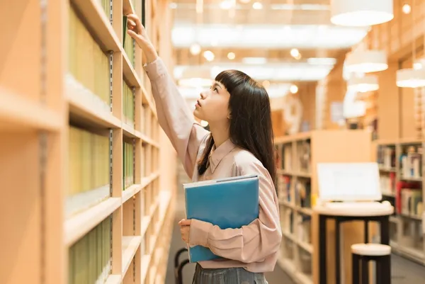 Female college student looking for a book in the l